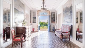A grand hallway with a view to a garden, ornate chairs, and a chandelier. - Château de Veullerot, with its ponds in the heart of Burgundy (Liernais)