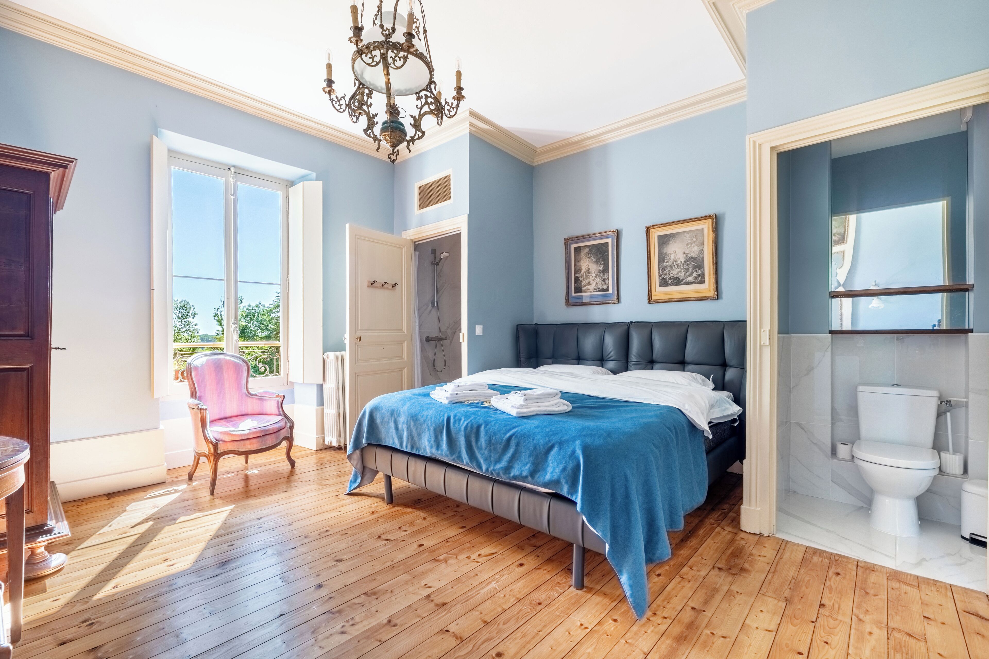 Une chambre à coucher avec un lit, une chaise, un lustre et une vue sur l’extérieur.