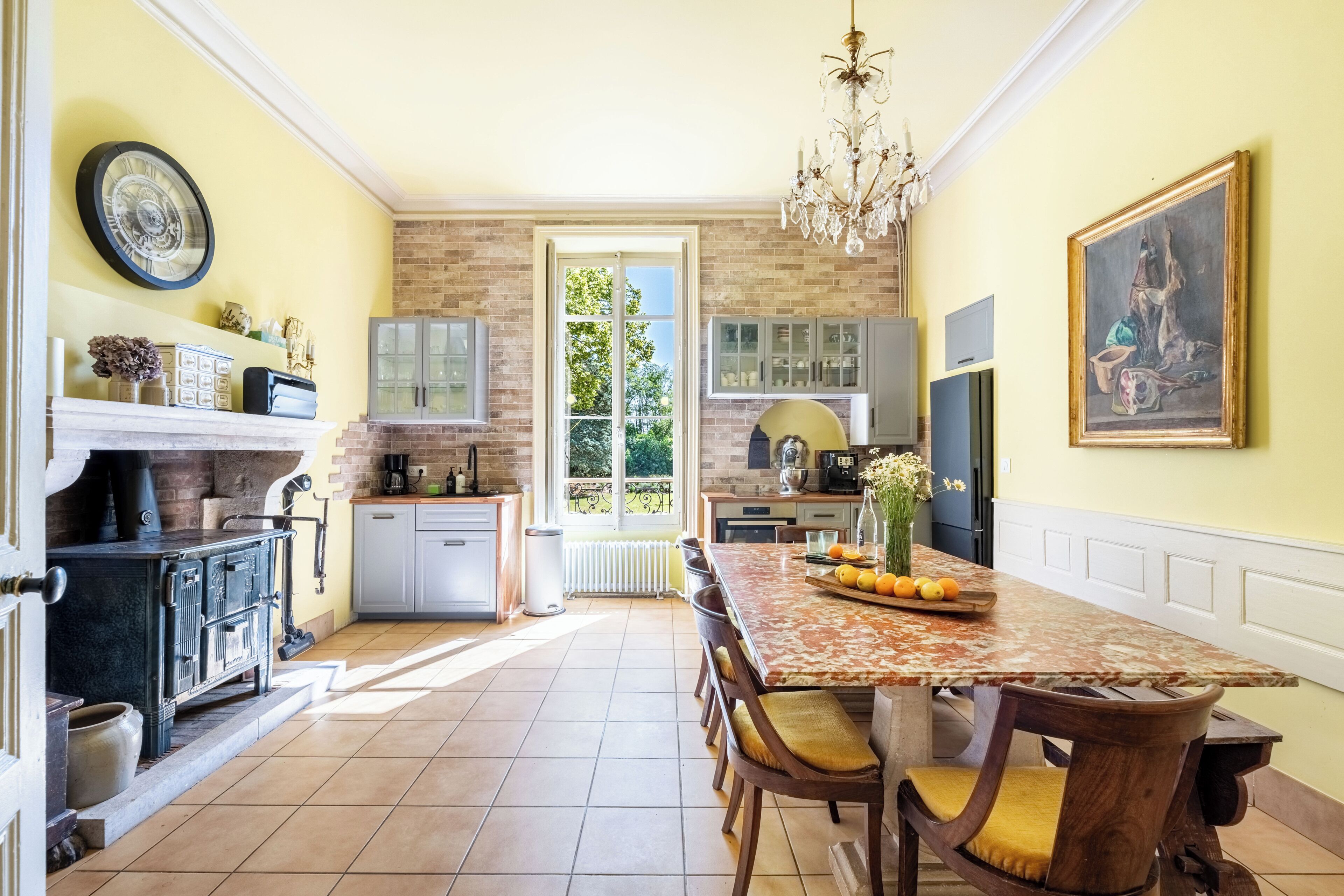 A kitchen with a dining table, chairs, a chandelier, and a painting on the wall.