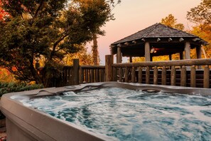 A hot tub with a wooden fence and a gazebo in the background.
