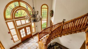 Un interior espacioso con una escalera de madera, ventanas arqueadas amplias y un candelabro.