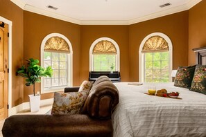 A bedroom with a large bed, a piano, and three arched windows with curtains.