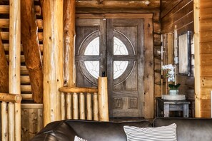 A log cabin interior with a wooden door, a cushioned sofa, and a small side table with a vase.