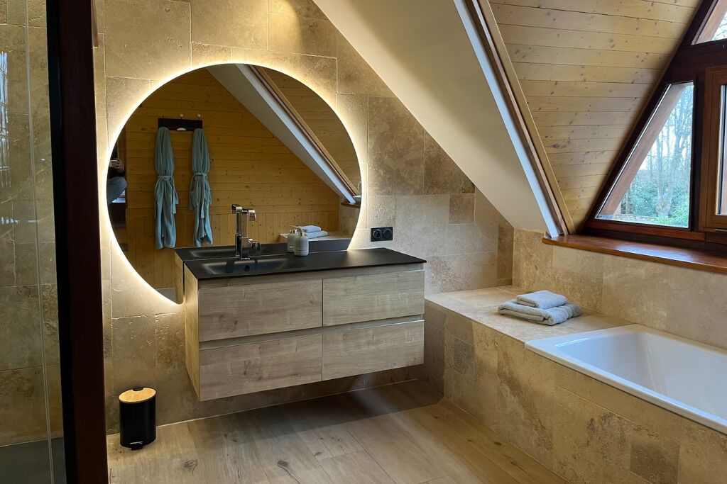 A modern bathroom with a skylight, a freestanding bathtub, and a vanity with a circular mirror.
