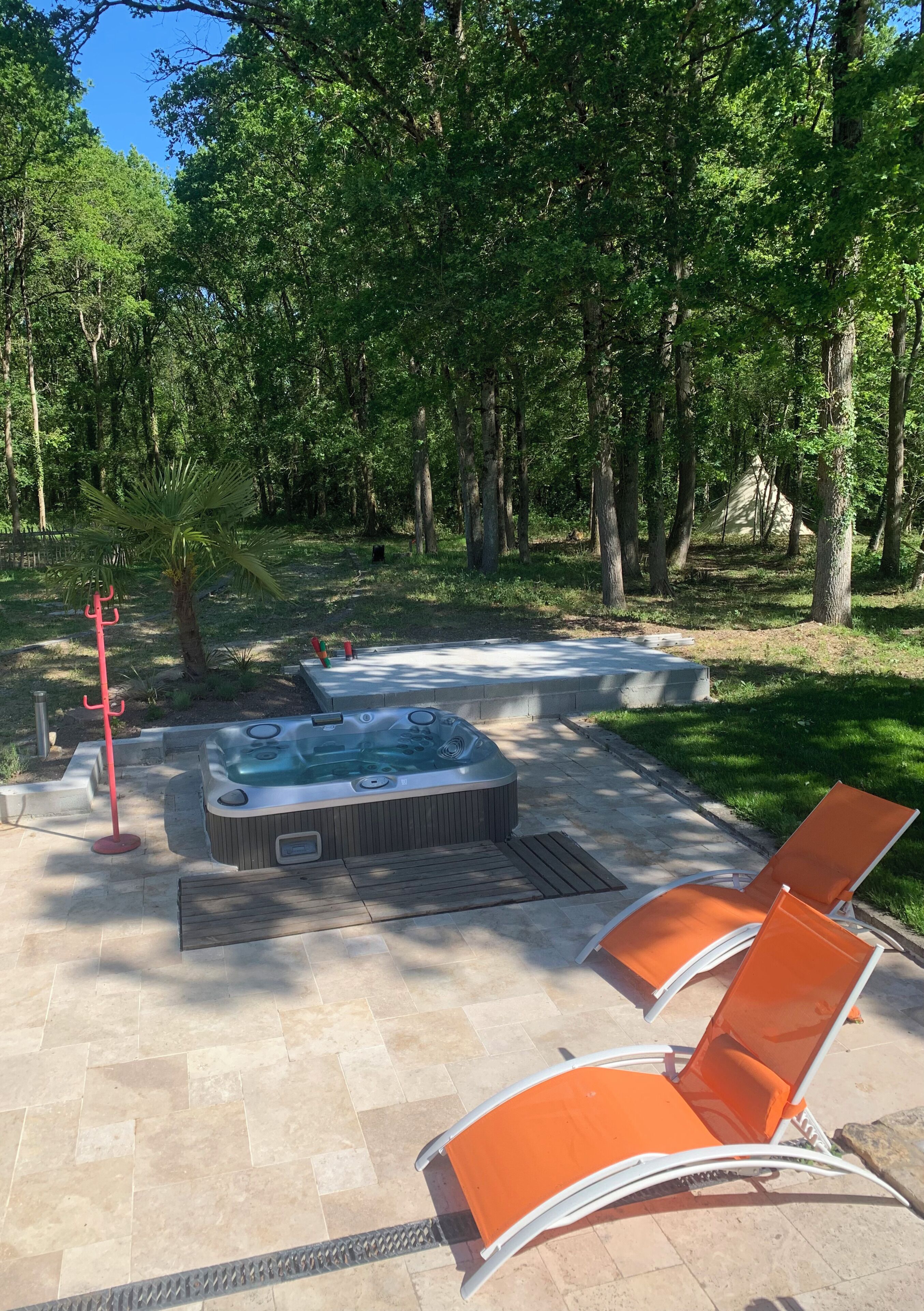 A hot tub in a forested area with two lounge chairs.