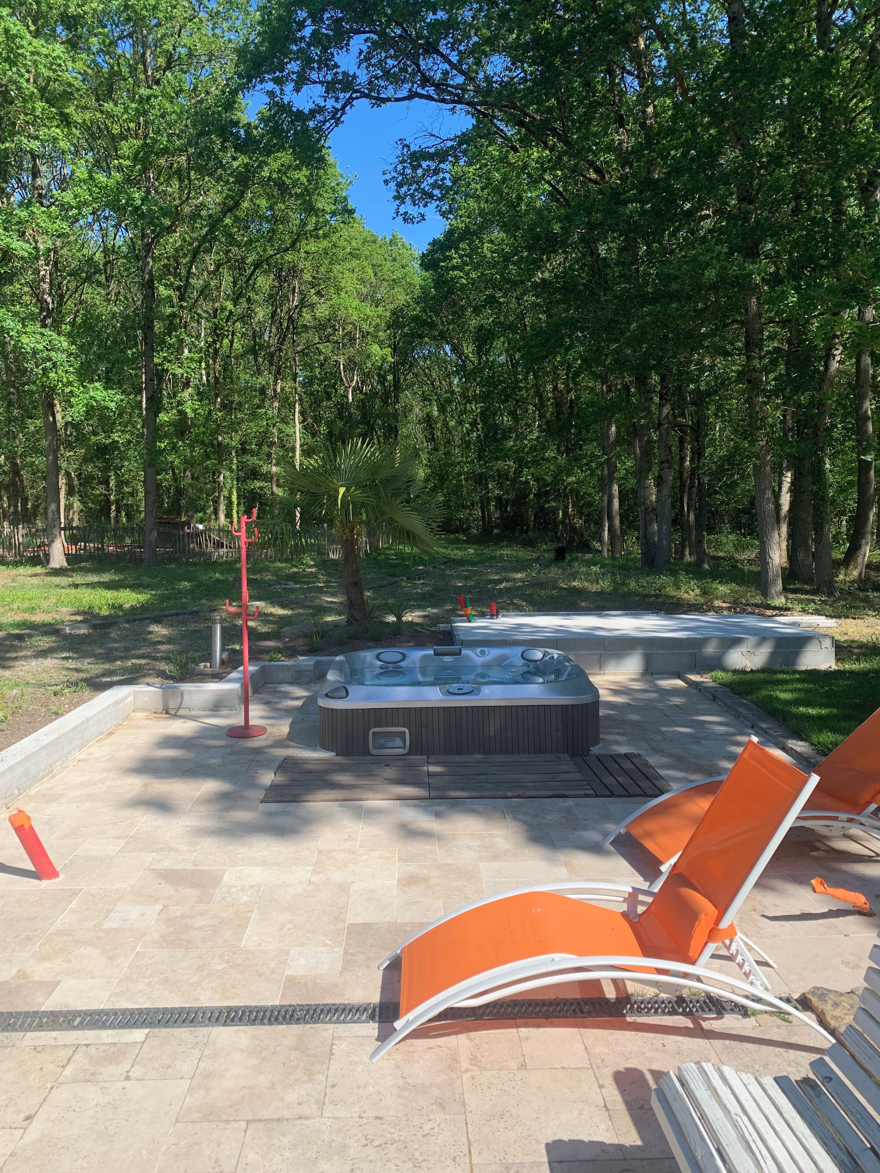 A hot tub surrounded by orange chairs, set in a forested area with a clear sky.