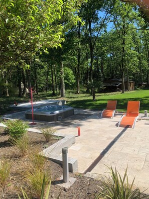 A hot tub surrounded by orange lounge chairs, a wooden deck, and a grassy area with trees. -  L’Atelier, cosy et moderne & terrasse avec jacuzzi (Rives-du-Loir-en-Anjou)