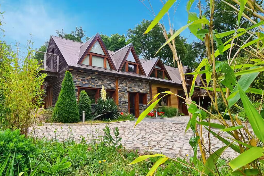 A rustic wooden house with a stone facade, a stone pathway, and a well-maintained garden.