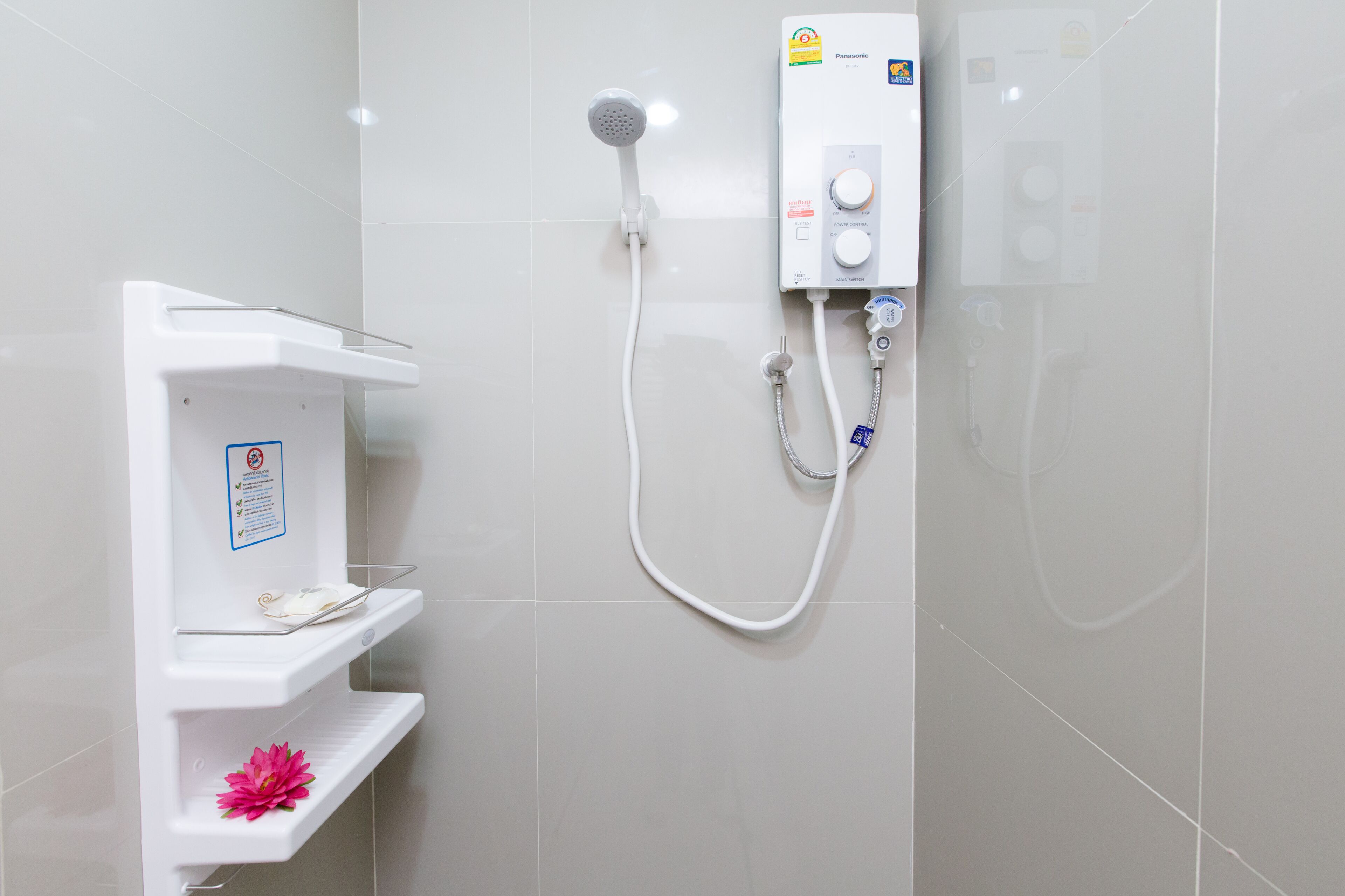 A bathroom with a white shower unit, a shelf with a pink flower, and a no-smoking sign.