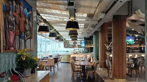 A modern restaurant with a wooden counter, dining tables, and hanging pendant lights. - Standard Apartment, Very Cosy and Stylish Suitable for a Romantic Outing (Johannesburg)