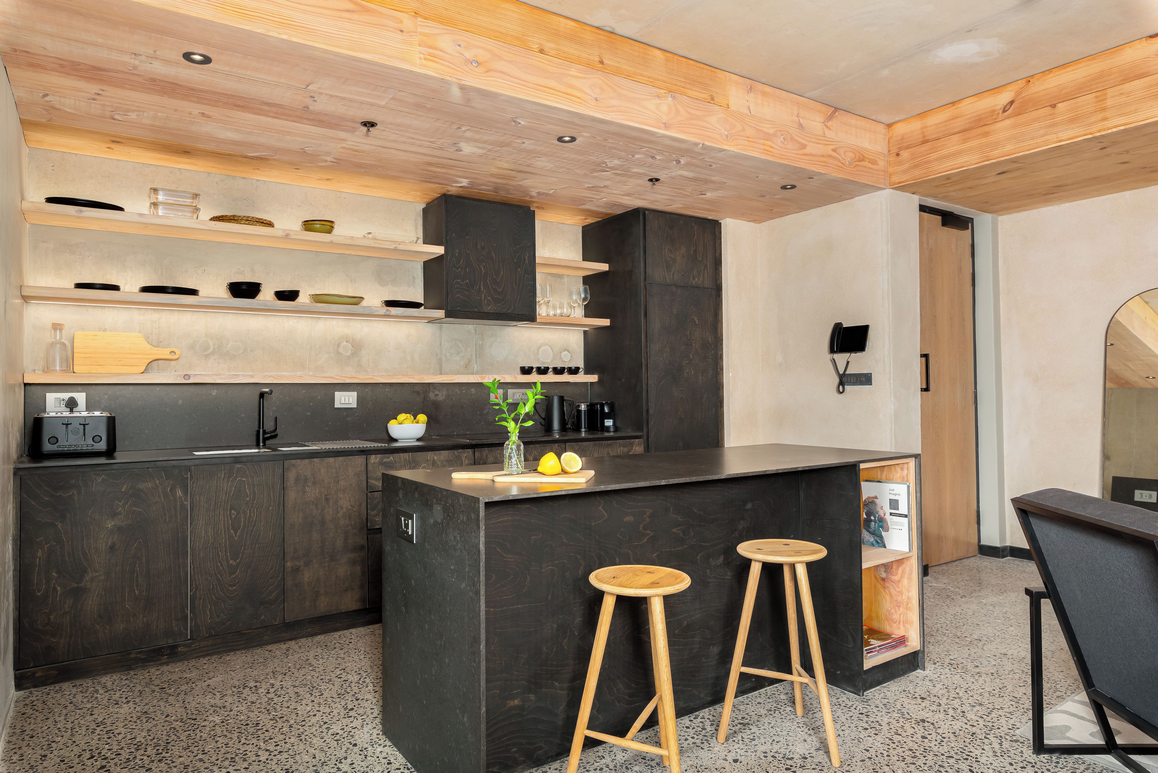 A modern kitchen with dark cabinetry, wooden countertops, and a central island with stools.