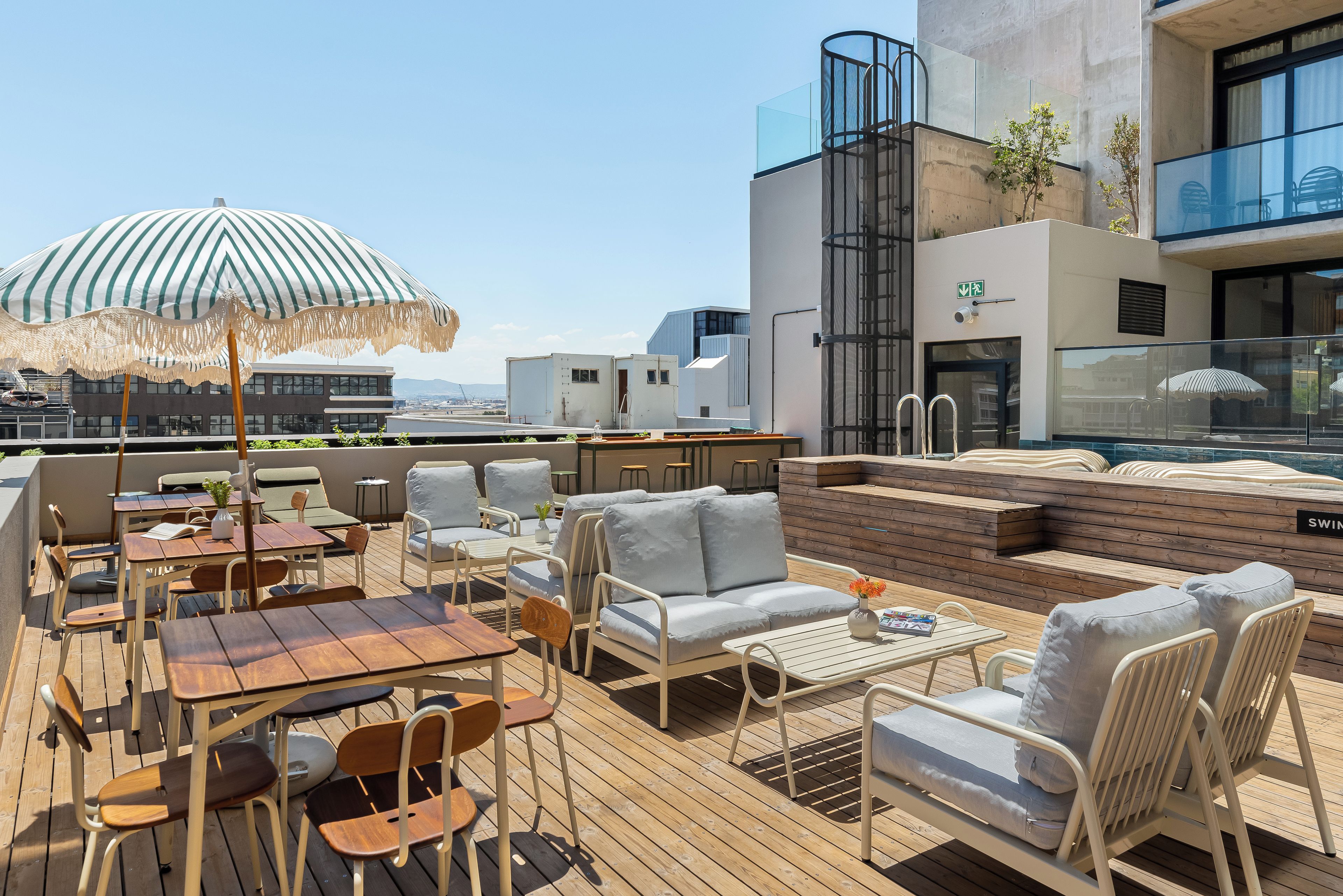 A rooftop terrace with outdoor seating, a large umbrella, and a view of the cityscape.