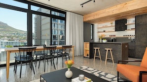 A modern apartment with a dining area, kitchen, and large windows offering a city view. - Neighbourgood Harrington (Cape Town)