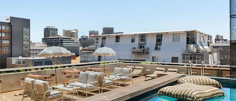 A rooftop pool area with lounge chairs and umbrellas, surrounded by modern buildings.