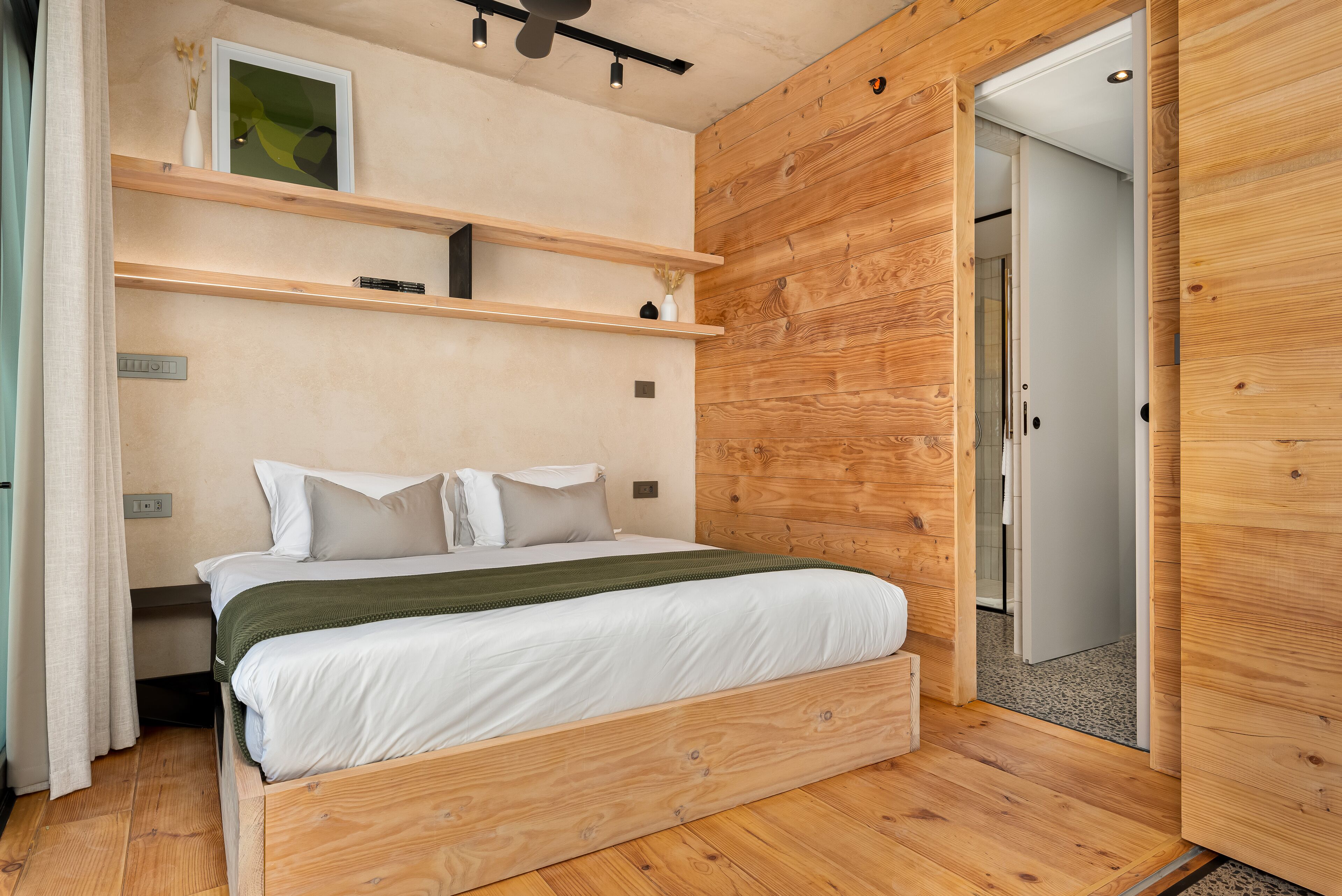 A modern bedroom with a wooden bed frame, white bedding, and built-in wooden shelves.