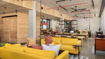 A modern interior with yellow sofas, wooden panel walls, and a mix of seating and workspaces.