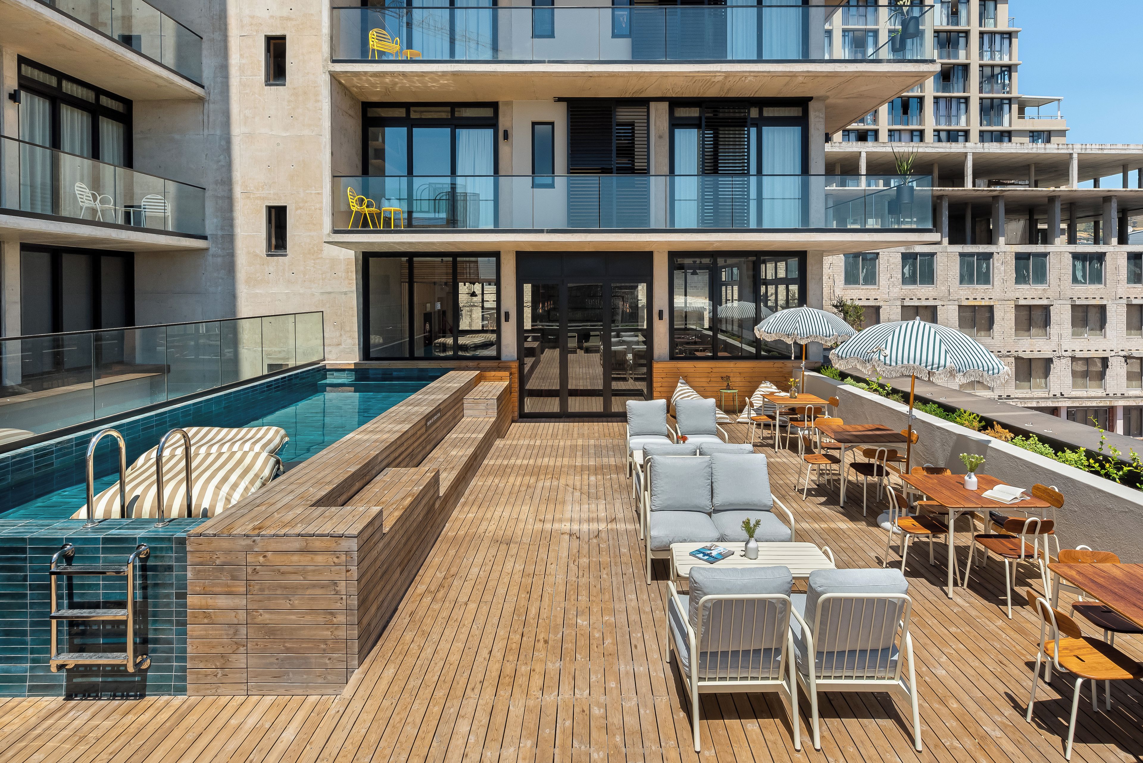 A rooftop pool area with a wooden deck, lounge chairs, and umbrellas.