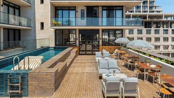 A rooftop pool area with a wooden deck, lounge chairs, and umbrellas.