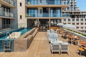 Uma área de piscina no terraço com deck de madeira, espreguiçadeiras e guarda-sóis.