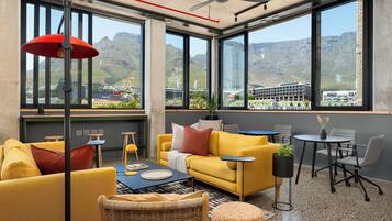 A modern interior with a yellow sofa, a small round table, and a view of mountains through large windows.