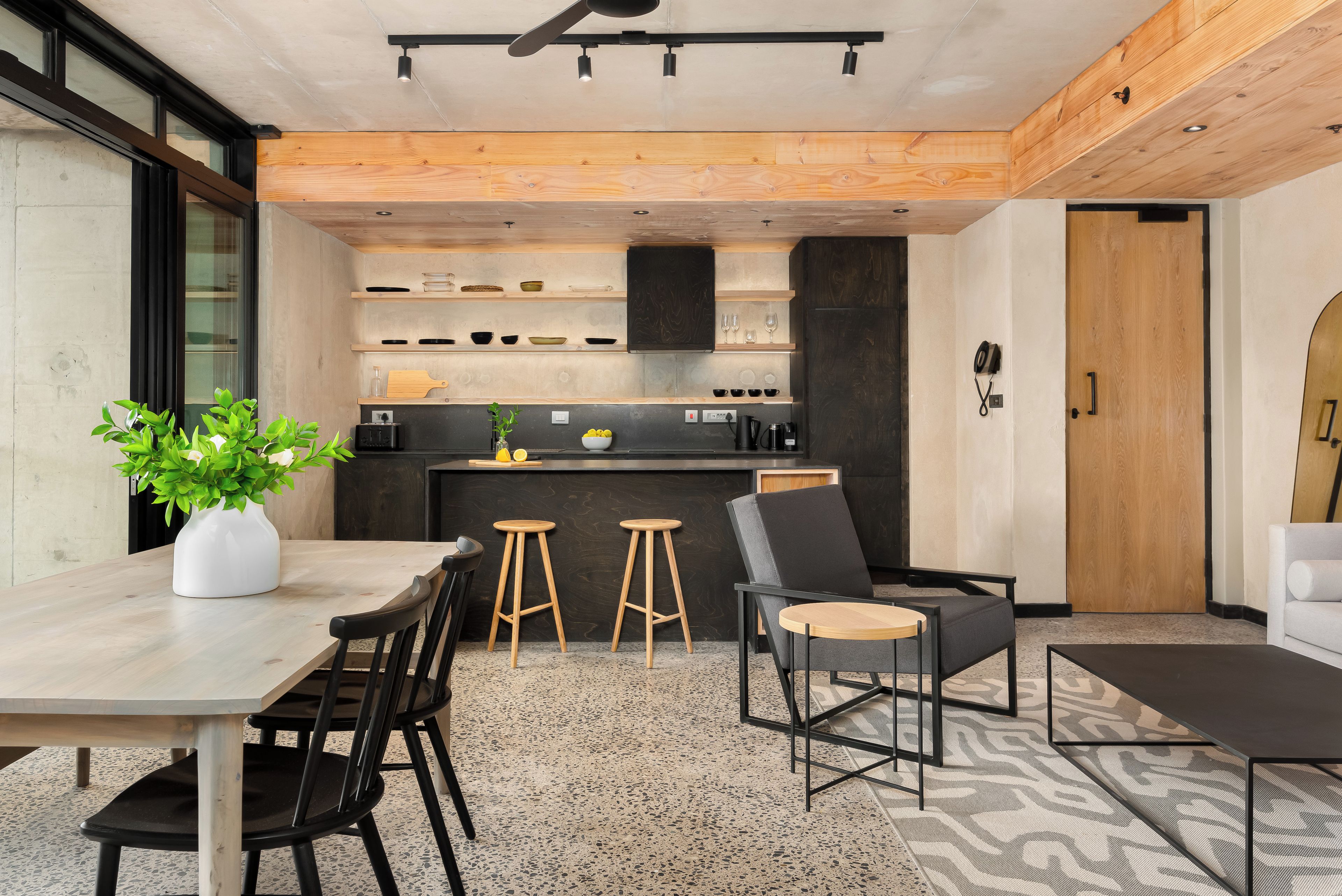 Una cocina moderna con estantes de madera, una zona de comedor con mesa y sillas, y un rincón de estar con sofá y sillones.