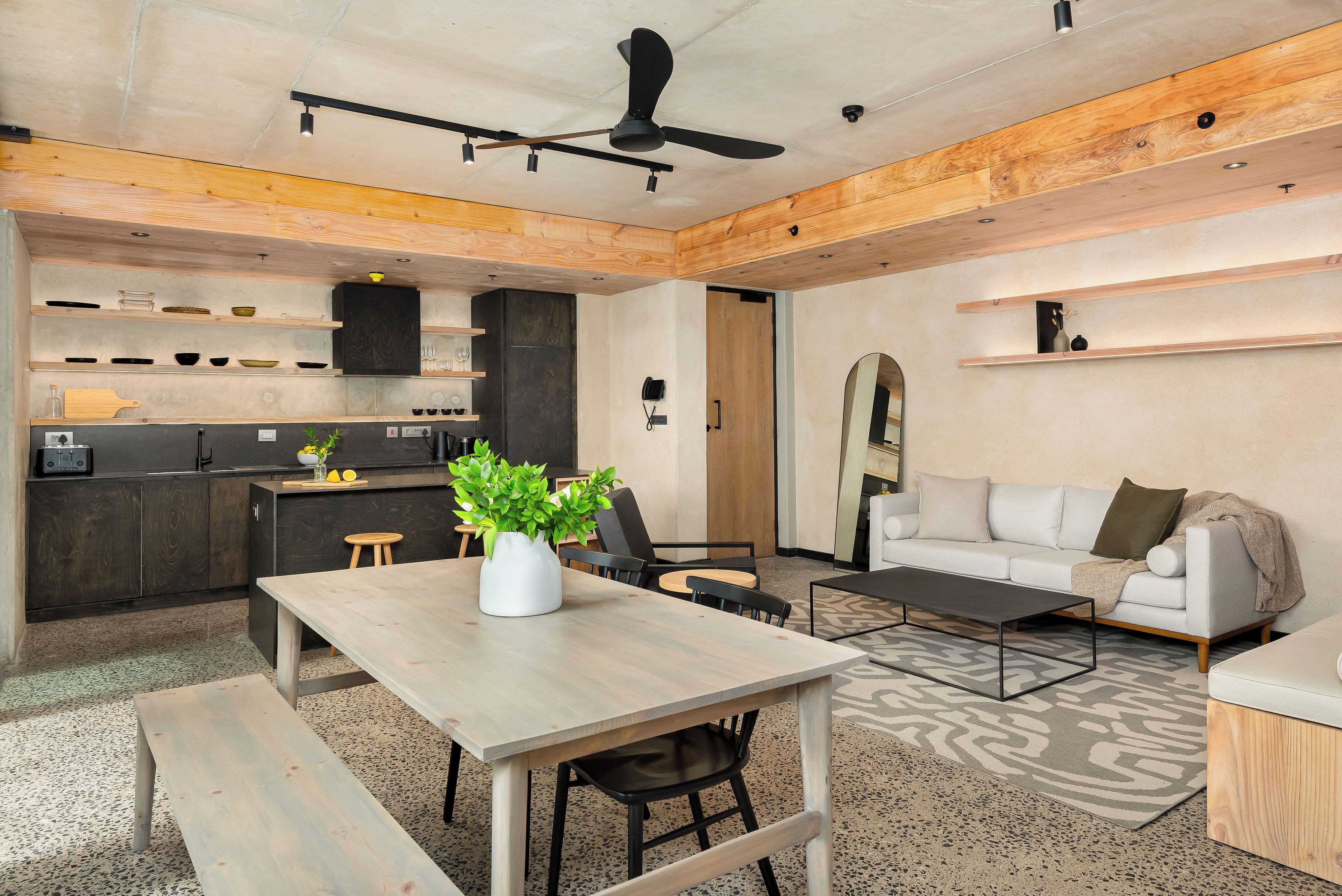 A modern kitchen with wooden cabinets, a dining table with chairs, a coffee table, and a sofa in a living area.