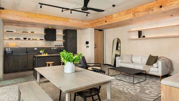 A modern kitchen with wooden cabinets, a dining table with chairs, a coffee table, and a sofa in a living area.