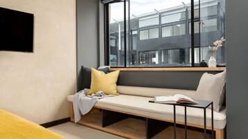 Une chambre moderne dotée d’une grande fenêtre, d’un banc avec des coussins, d’un téléviseur à écran plat et d’une petite table sur laquelle est posé un livre.