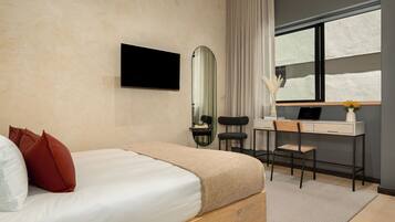 A bedroom with a bed, a desk, a chair, a mirror, and a window.