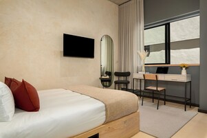 A bedroom with a bed, a desk, a chair, a mirror, and a window.