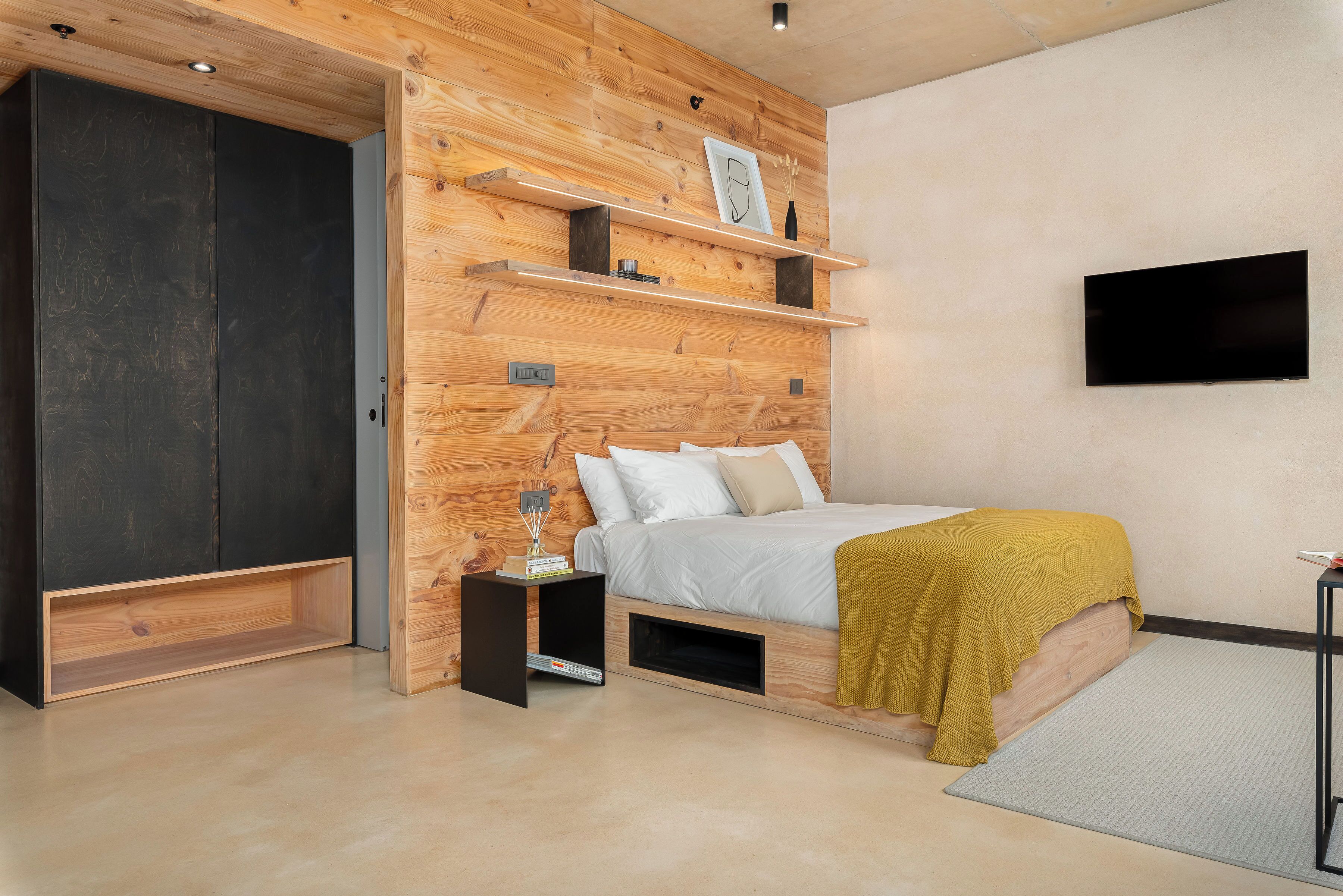 A modern bedroom with a bed, wooden shelves, a TV, and a wardrobe.