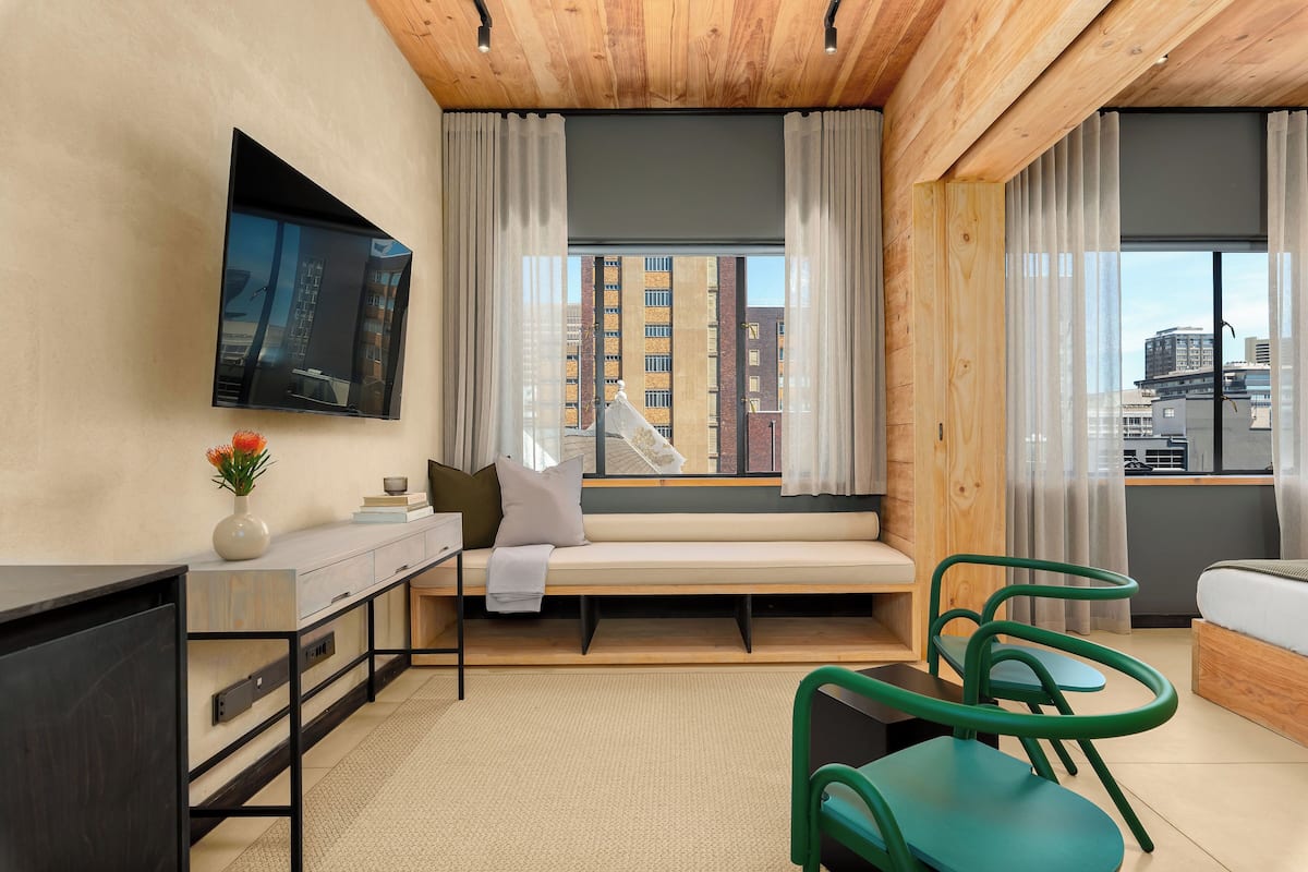 Una habitación de hotel moderna con un ventanal grande, un sofá, un escritorio y un televisor montado en la pared.