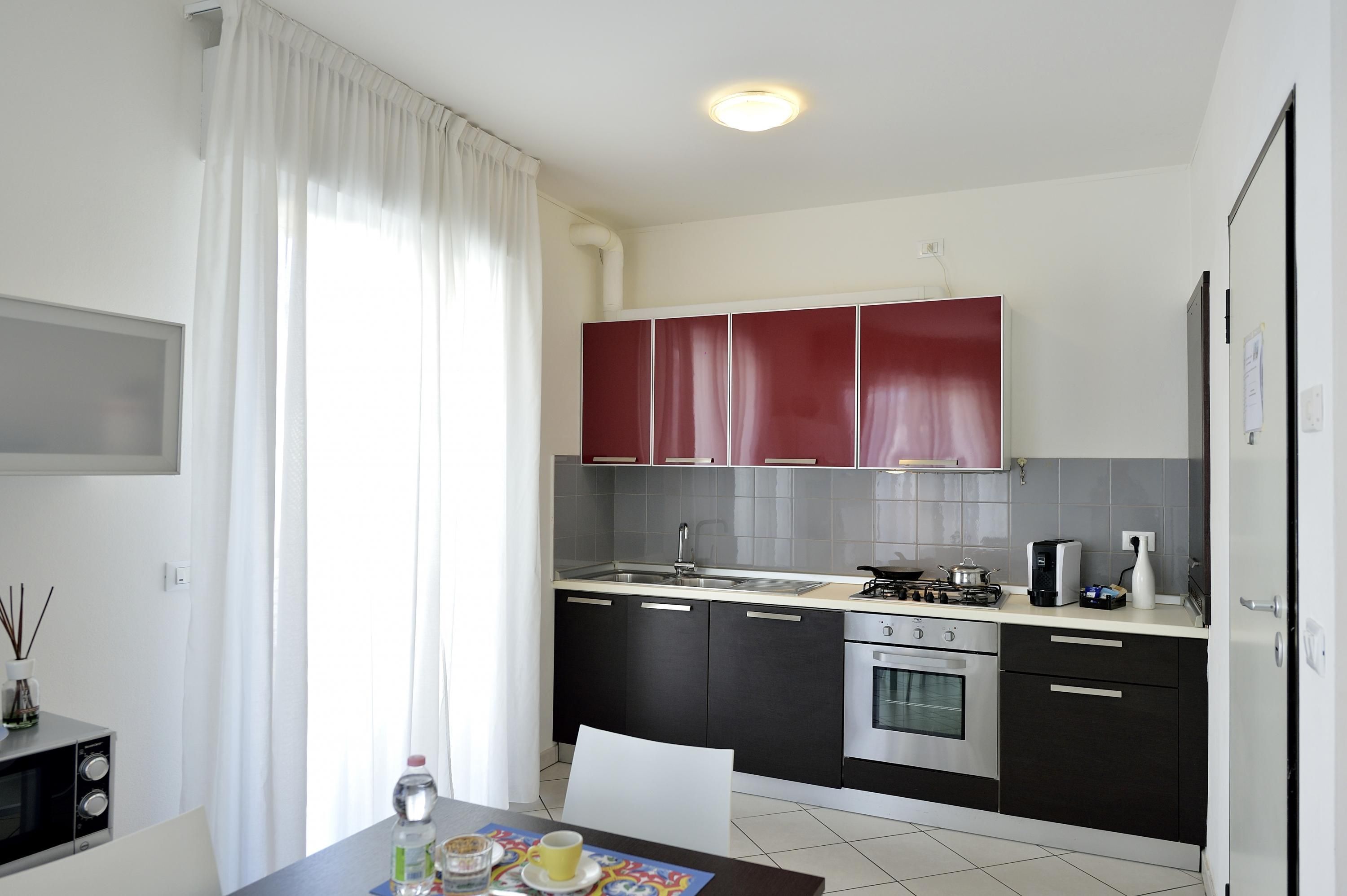A modern kitchen with black and red cabinets, a stainless steel sink, and a gas stove.