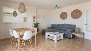 A living room with a sofa, coffee table, dining table with chairs, and decorative woven wall hangings. - Villa Ocean Breeze - Steps away from the Beach (San Jaime Mediterráneo)