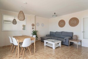 A living room with a sofa, coffee table, dining table with chairs, and decorative woven wall hangings.
