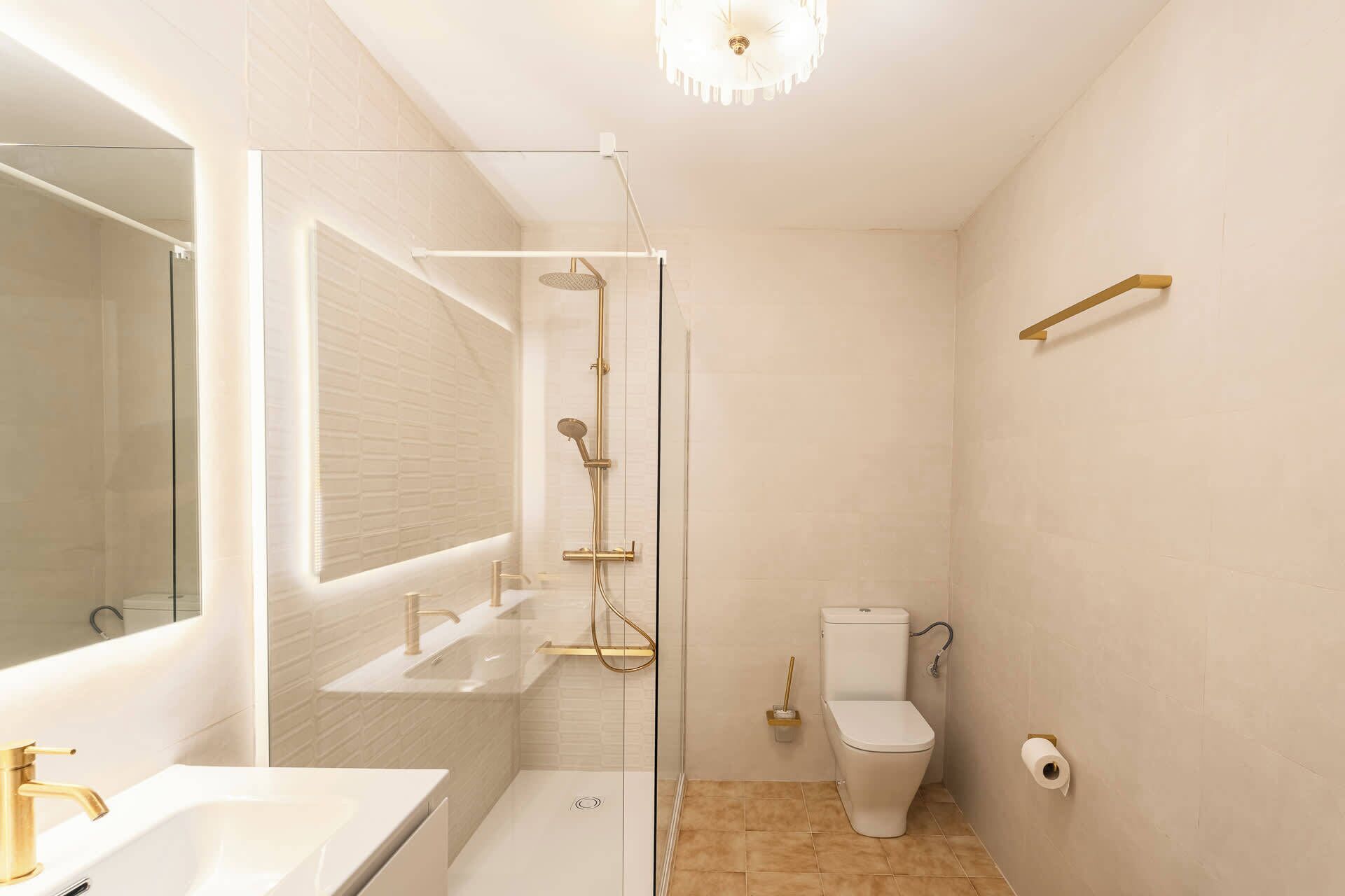A modern bathroom with a glass shower enclosure, a white toilet, and a sink with a gold faucet.