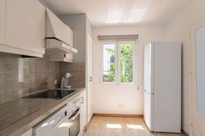 A kitchen with a built-in oven, a refrigerator, and a window with a view of greenery.