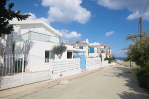 Un quartier résidentiel situé sur la côte, avec des bâtiments blancs, une porte bleue et un ciel dégagé.
