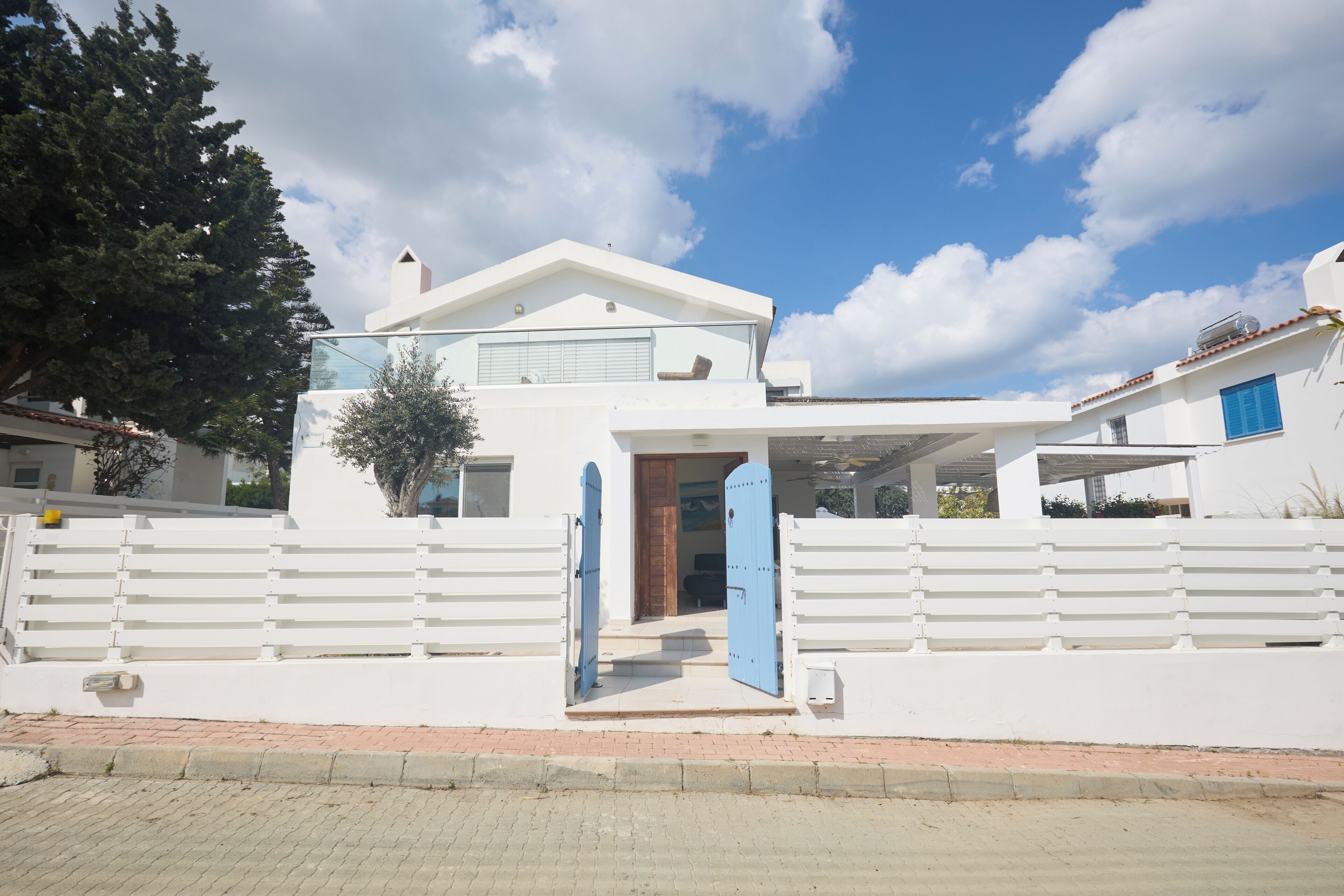 Une maison moderne, blanche, avec une porte bleue, un porche couvert et une clôture blanche.