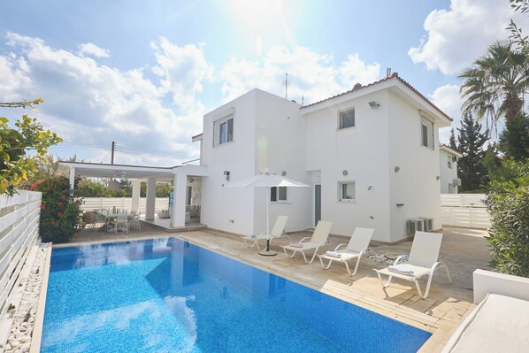 Une maison blanche à deux étages, dotée d’une piscine, d’un espace salon extérieur et d’une pergola.
