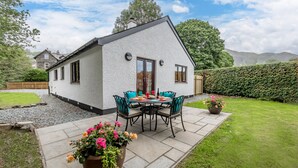 Een wit huis met een terras, een tafel met stoelen en een grote bloempot.