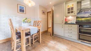 Een moderne keuken met witte kastjes, een houten eettafel en een hanglamp.