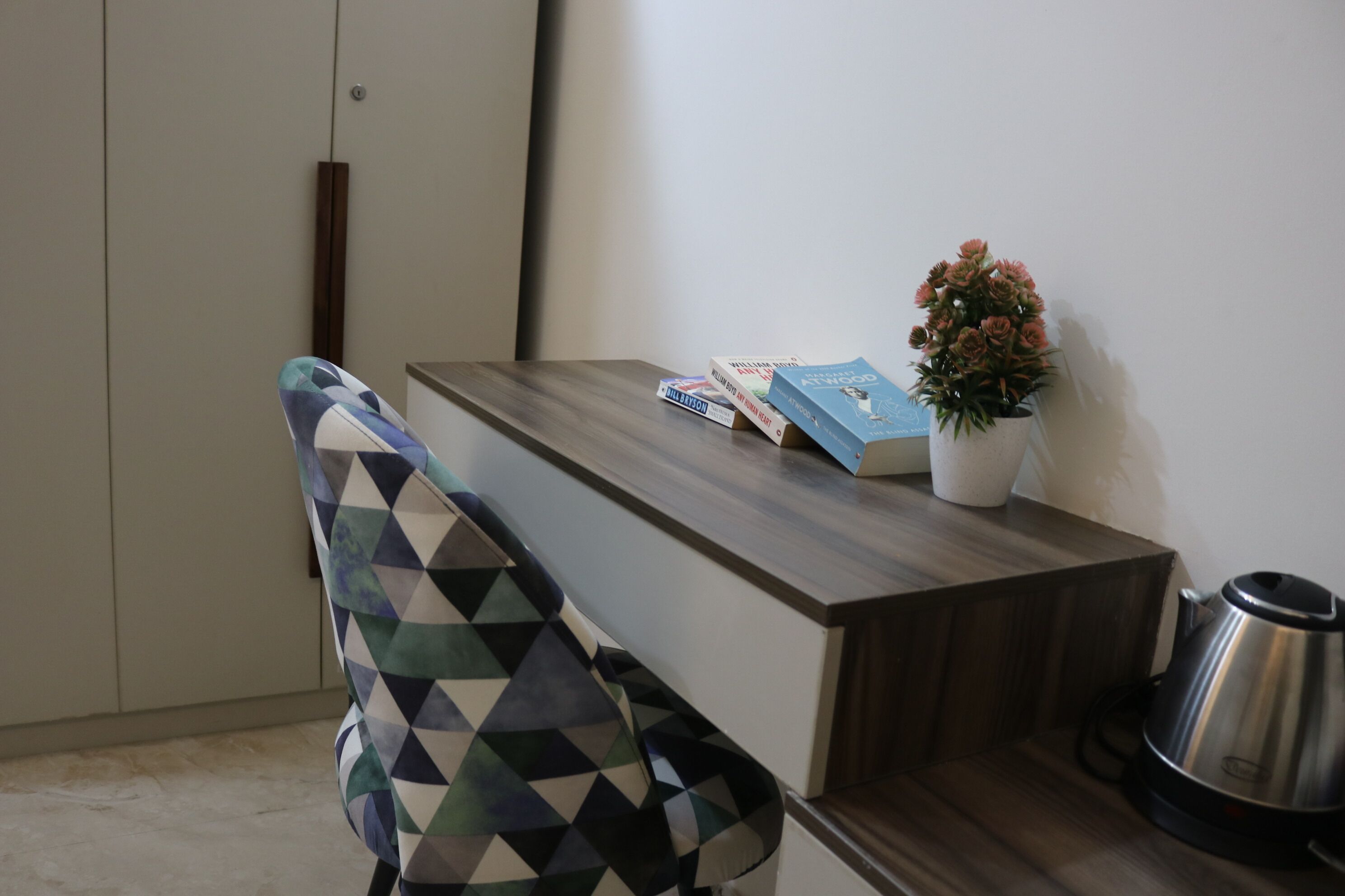 A modern room with a wooden desk, a patterned chair, a potted plant, and a kettle.