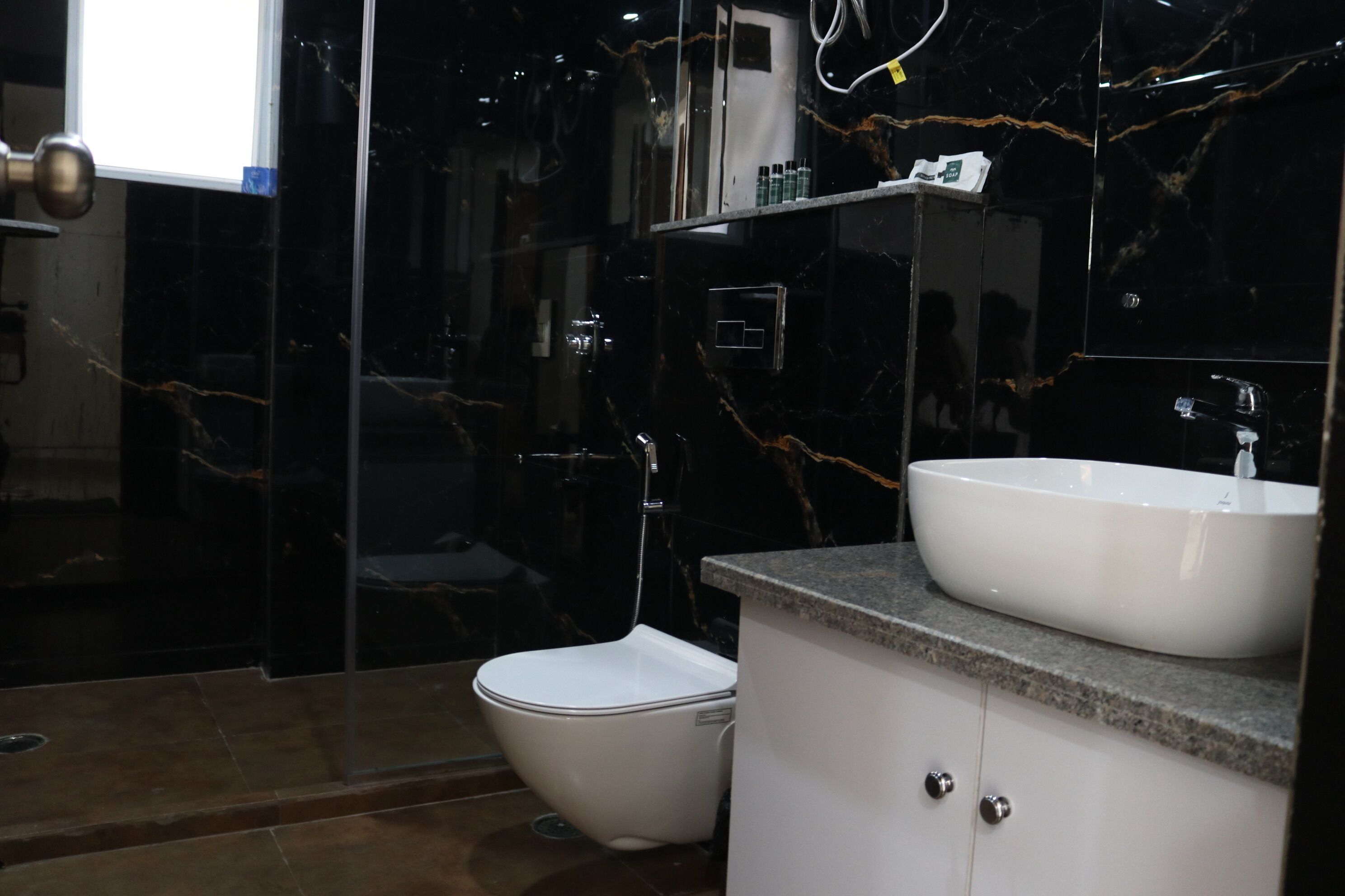 A modern bathroom with a white toilet, a large mirror, and a white sink on a granite countertop.