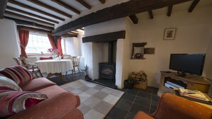A cozy living room with a fireplace, a television, and a dining area with a table and chairs. - Tarn Foot Cottage, Duddon Valley, Lake District  - A rural retreat set deep within the spectacular D (Seathwaite)