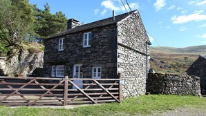 A stone house with a wooden gate, surrounded by greenery and hills in the background. - Tarn Foot Cottage, Duddon Valley, Lake District  - A rural retreat set deep within the spectacular D (Seathwaite)
