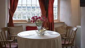 A round dining table with a white tablecloth, surrounded by wooden chairs with cushions. A vase with pink flowers is placed on the table. - Tarn Foot Cottage, Duddon Valley, Lake District  - A rural retreat set deep within the spectacular D (Seathwaite)