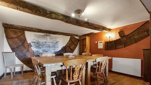 Een landelijke eetkamer met een houten tafel en stoelen, zichtbare balken en een groot schilderij aan de wand.