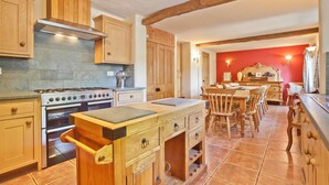 A kitchen with wooden cabinets, a stove, and a dining area with a red wall. - Sleeps 12 guests in 6 bedrooms with 2 hot tubs (Coniston)
