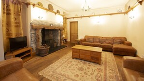 A cozy living room with a fireplace, a sofa, a television, and a wooden coffee table. - Sleeps 12 guests in 6 bedrooms with 2 hot tubs (Coniston)